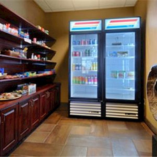 The image shows a small convenience store or snack bar with shelves of various items and a refrigerator containing drinks and perishable goods.