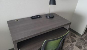 A desk setup featuring a lamp, an electrical outlet, a chair tucked in, and a portion of wall art visible above the desk.